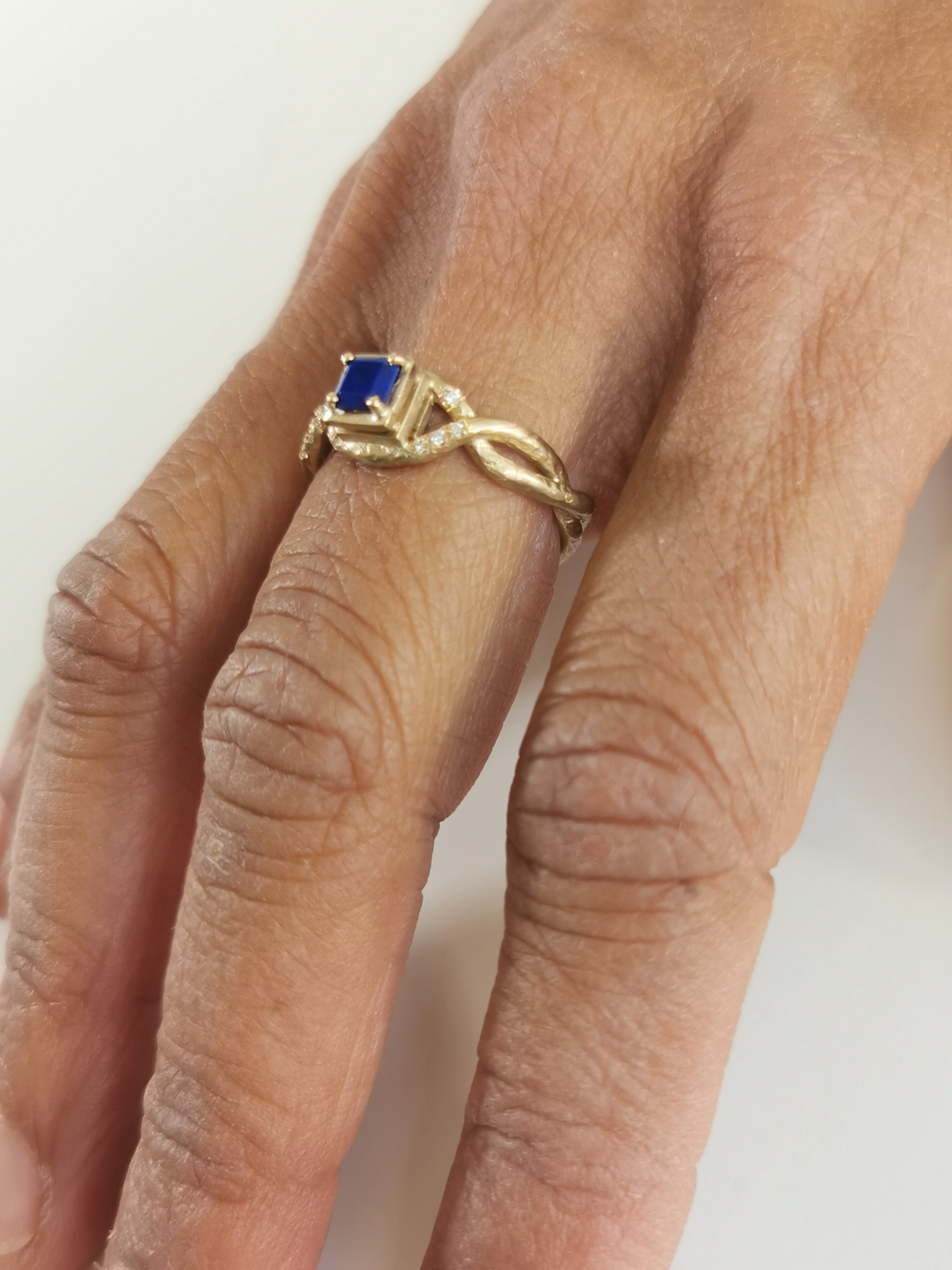 Custom gold gemstone ring with square blue stone and handmade gold band on hand.